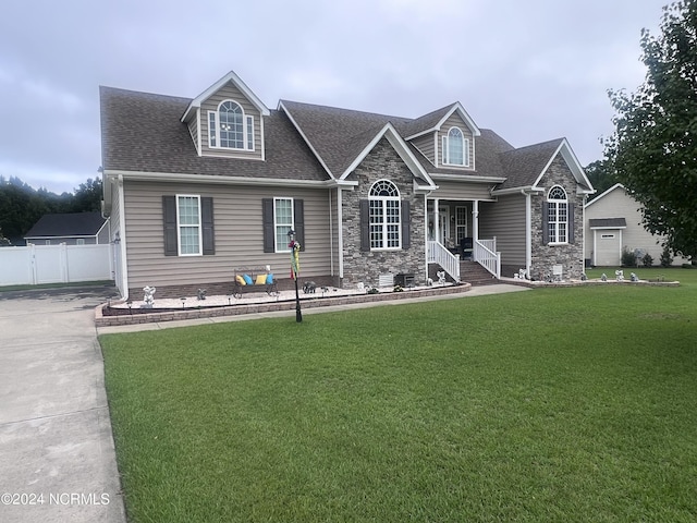 view of front of house with a shingled roof, stone siding, fence, and a front lawn