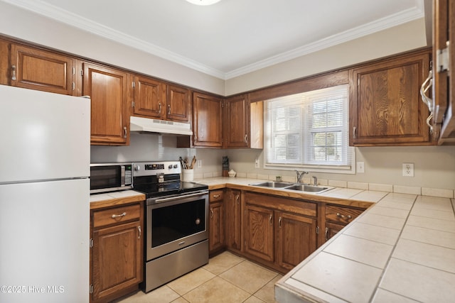 kitchen with under cabinet range hood, a sink, ornamental molding, appliances with stainless steel finishes, and tile counters