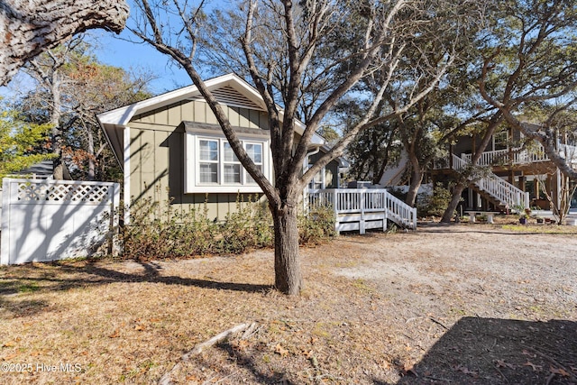 view of property exterior with board and batten siding, fence, a wooden deck, and stairs