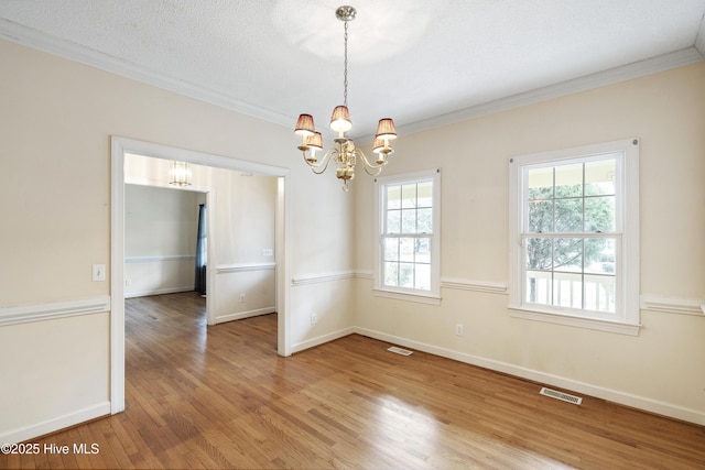 unfurnished dining area with crown molding, light wood-style flooring, visible vents, and a notable chandelier