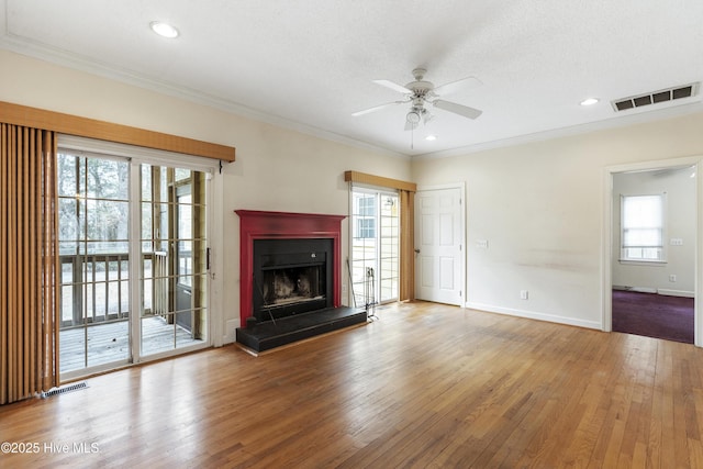 unfurnished living room featuring crown molding, visible vents, a fireplace with raised hearth, and hardwood / wood-style floors