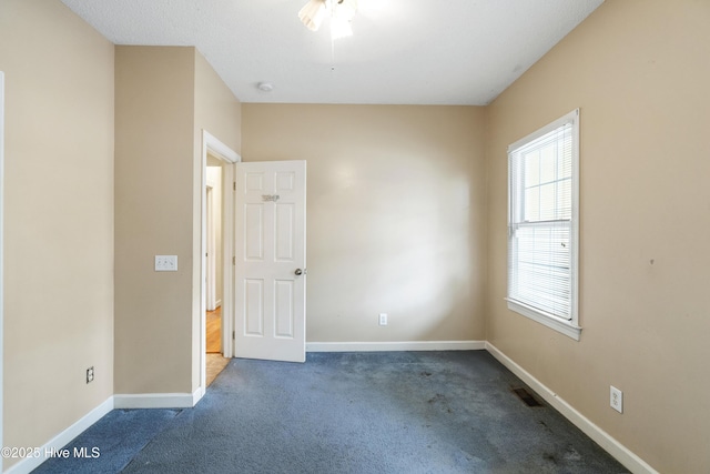 empty room with dark colored carpet, visible vents, and baseboards