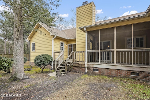 rear view of property with a sunroom, crawl space, a shingled roof, and a chimney