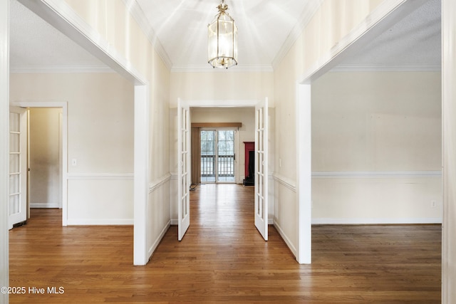 corridor with crown molding, wood finished floors, baseboards, french doors, and an inviting chandelier