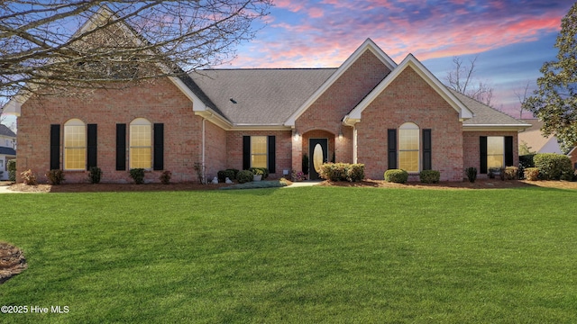 view of front of property with brick siding, roof with shingles, and a yard