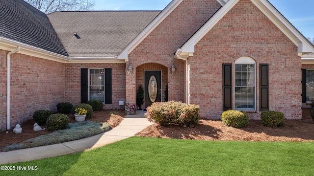 view of front of home featuring a front yard, brick siding, and roof with shingles