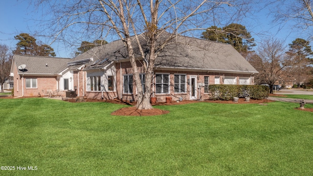 view of front of house featuring brick siding, roof with shingles, and a front yard