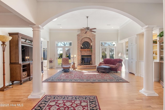 living area featuring a healthy amount of sunlight, light wood finished floors, a brick fireplace, and ornamental molding