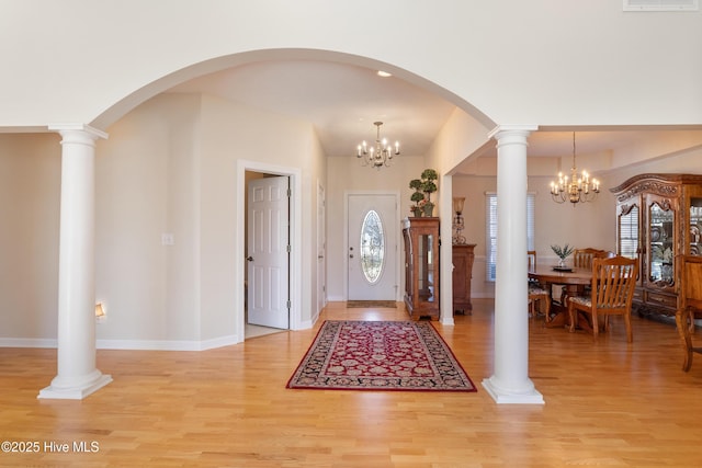 foyer entrance with light wood-type flooring, a notable chandelier, decorative columns, and baseboards