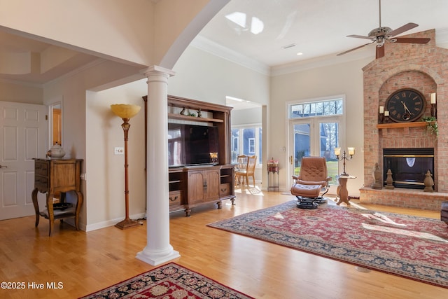 living room with a fireplace, wood finished floors, baseboards, ornate columns, and crown molding