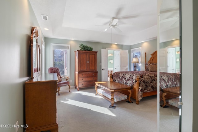 bedroom with a tray ceiling, light colored carpet, visible vents, and baseboards