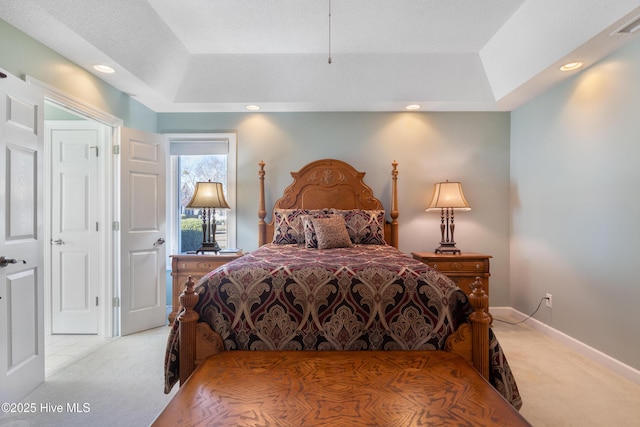 bedroom with a raised ceiling, light carpet, and baseboards