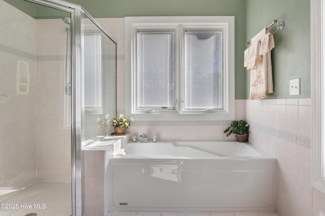 full bathroom with tile walls, a garden tub, and a shower stall