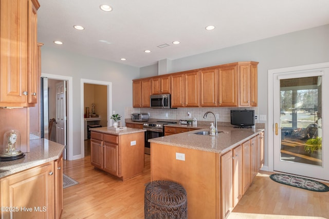 kitchen with light stone counters, appliances with stainless steel finishes, a sink, light wood-style floors, and backsplash