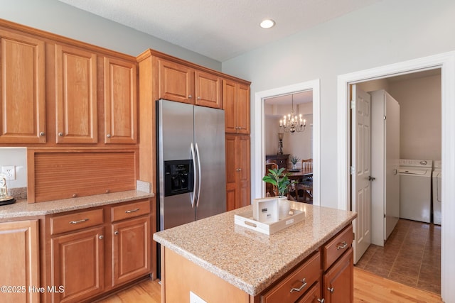 kitchen with a center island, washer and clothes dryer, brown cabinetry, light stone countertops, and stainless steel fridge with ice dispenser