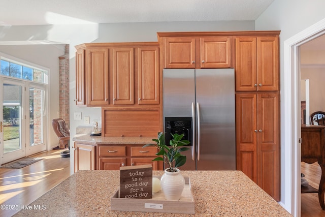 kitchen featuring light stone counters, brown cabinetry, wood finished floors, and stainless steel fridge with ice dispenser