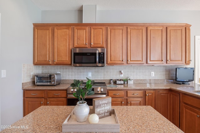 kitchen with a toaster, decorative backsplash, appliances with stainless steel finishes, brown cabinets, and light stone counters