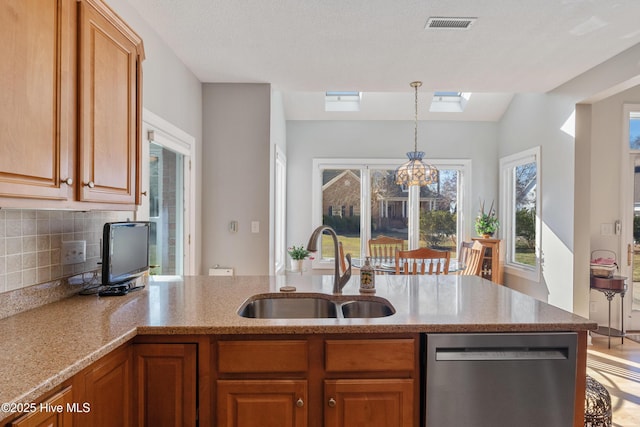 kitchen with a skylight, a sink, stainless steel dishwasher, light stone countertops, and brown cabinetry