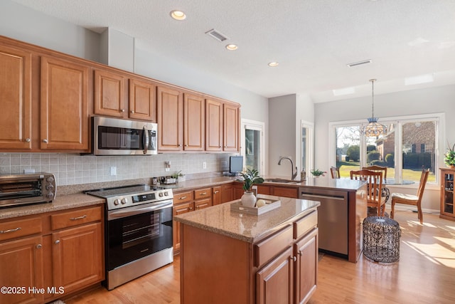 kitchen with visible vents, decorative backsplash, a peninsula, stainless steel appliances, and a sink