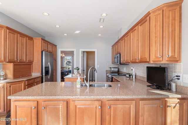 kitchen with a peninsula, appliances with stainless steel finishes, a sink, and light stone counters