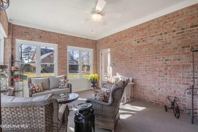 carpeted living room featuring a ceiling fan, crown molding, and brick wall