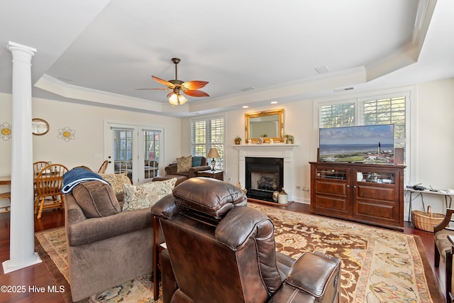 living area featuring ornate columns, a fireplace, a tray ceiling, and wood finished floors