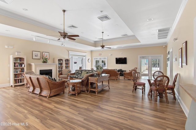 living area with a tray ceiling, a fireplace, wood finished floors, and visible vents