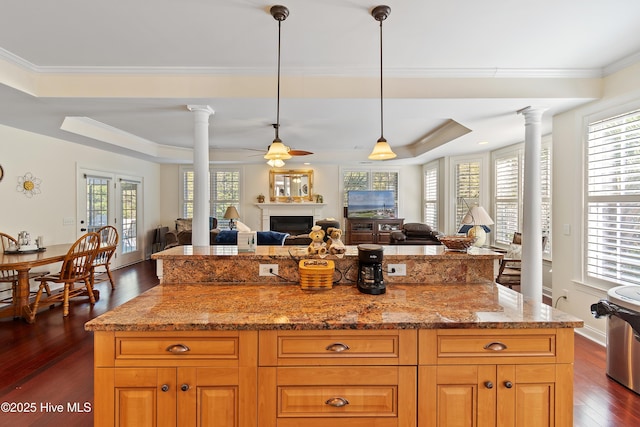 kitchen featuring a raised ceiling, open floor plan, dark wood-type flooring, ornate columns, and a fireplace