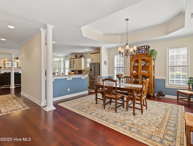 dining room with dark wood-style floors, a tray ceiling, a wealth of natural light, and ornate columns