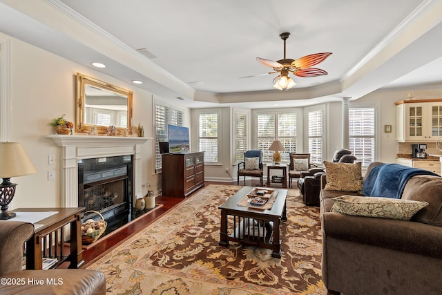 living area featuring a premium fireplace, wood finished floors, a ceiling fan, a tray ceiling, and crown molding