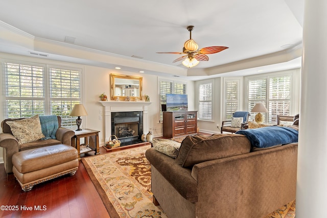 living area featuring visible vents, dark wood finished floors, a tray ceiling, crown molding, and a high end fireplace