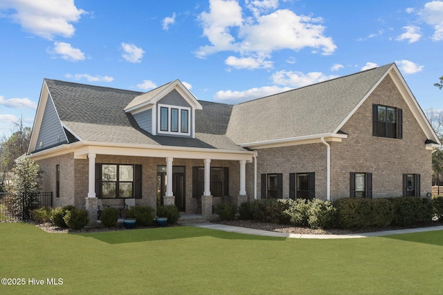 view of front of home with a front yard, brick siding, covered porch, and roof with shingles