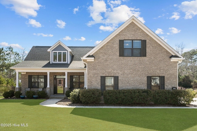 view of front facade featuring a front yard, a porch, brick siding, and roof with shingles