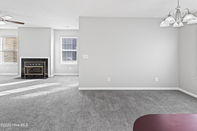 unfurnished living room featuring ceiling fan with notable chandelier, a fireplace, carpet flooring, and baseboards