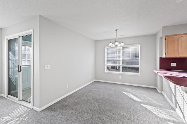 unfurnished dining area with a textured ceiling, baseboards, carpet flooring, and a notable chandelier