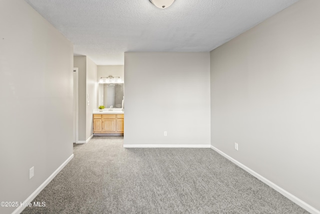 carpeted empty room featuring a textured ceiling, a sink, and baseboards