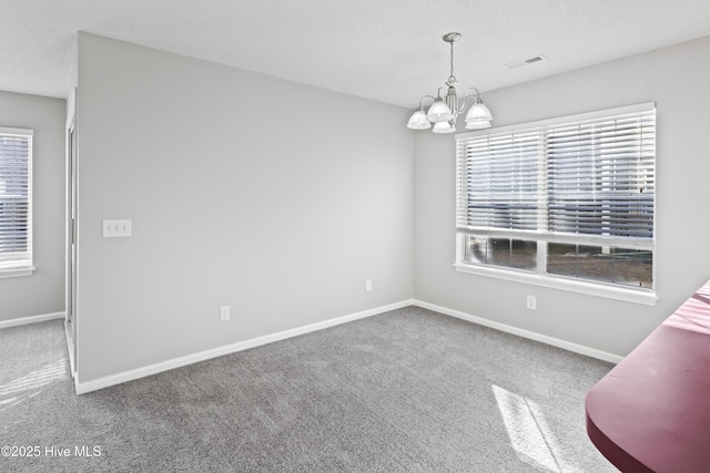 spare room featuring a notable chandelier, visible vents, carpet flooring, a textured ceiling, and baseboards