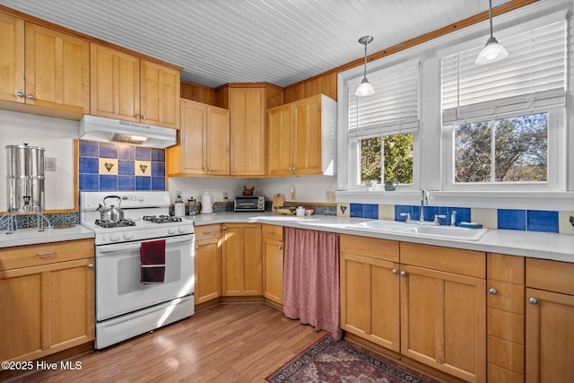 kitchen featuring white gas range oven, under cabinet range hood, a sink, and light countertops