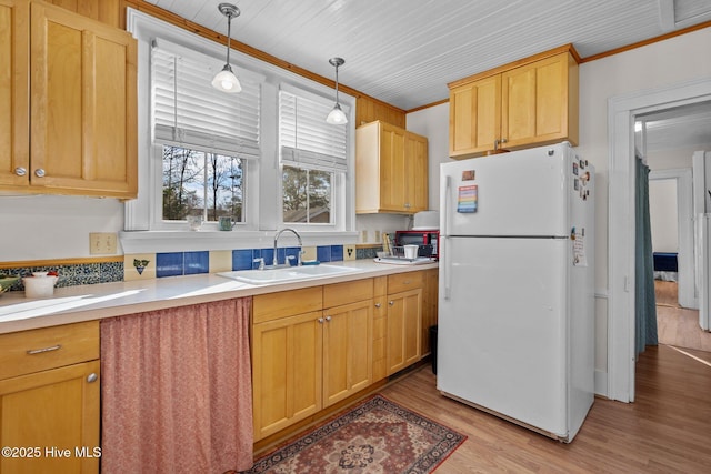 kitchen with freestanding refrigerator, a sink, light wood-style flooring, light countertops, and decorative light fixtures
