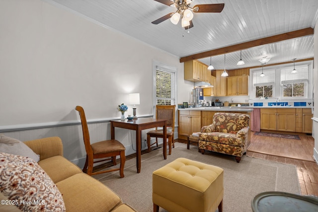 living area with a ceiling fan, a wainscoted wall, beam ceiling, light wood-style flooring, and wood ceiling