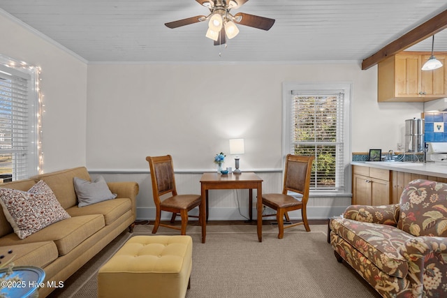 living area featuring light carpet, a ceiling fan, ornamental molding, and wainscoting