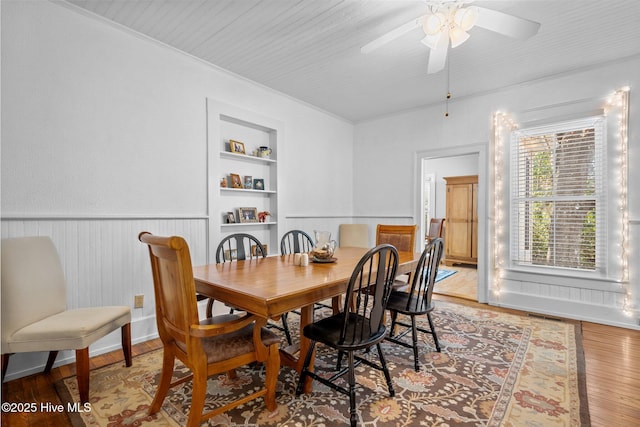 dining area featuring light wood-style flooring, wainscoting, ceiling fan, built in shelves, and ornamental molding