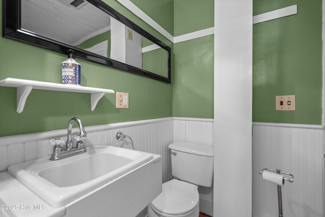 half bathroom featuring a wainscoted wall, a sink, and toilet