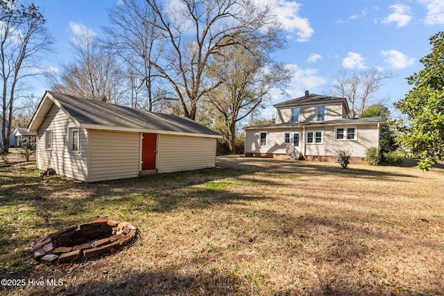 back of property featuring an outdoor fire pit, a lawn, and an outbuilding