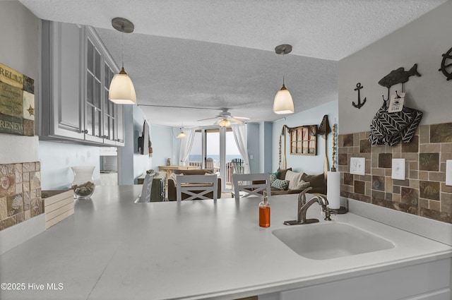 kitchen featuring decorative light fixtures, a sink, light countertops, a textured ceiling, and backsplash