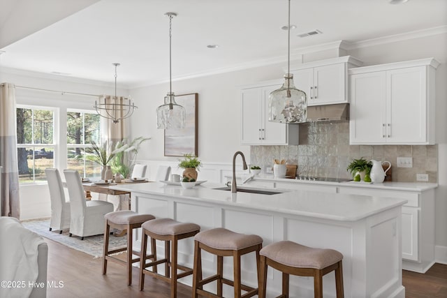 kitchen with light countertops, hanging light fixtures, a sink, and a kitchen island with sink