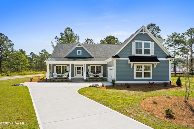 view of front of house featuring concrete driveway, metal roof, covered porch, a standing seam roof, and a front yard