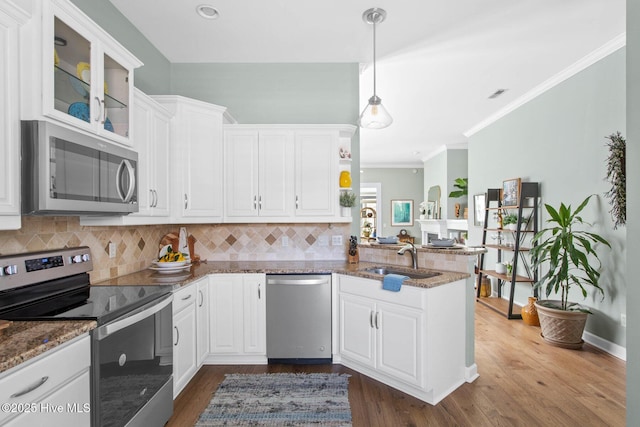 kitchen featuring white cabinets, appliances with stainless steel finishes, a peninsula, a sink, and backsplash