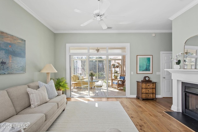 living room with a fireplace with flush hearth, a ceiling fan, ornamental molding, wood finished floors, and baseboards