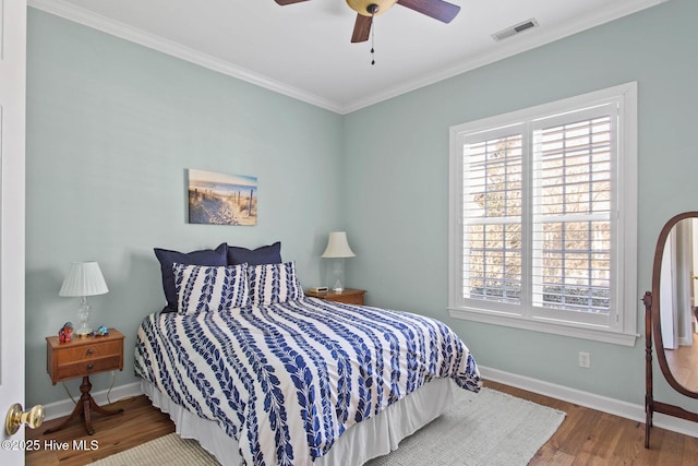 bedroom with crown molding, wood finished floors, visible vents, and baseboards